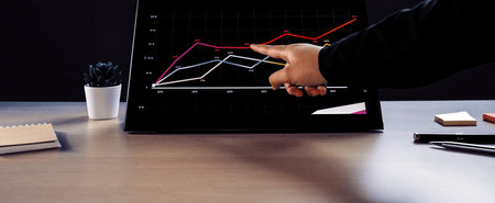 A businessperson interacts with a touchscreen device displaying colorful data graphs in a stylish...