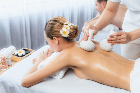 Hot herbal ball spa massage body treatment, masseur gently compresses herb bag on couple customer body. Tranquil and serenity of aromatherapy recreation in day lighting ambient at spa salon. Quiescentの写真素材