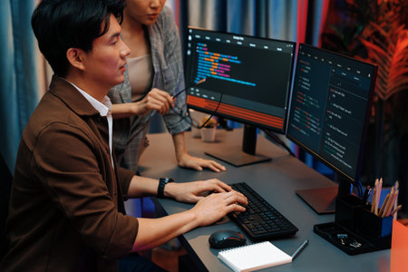 IT developers discussing with point to intelligent system running data online two screens information technology at neon light room at modern office.の写真素材