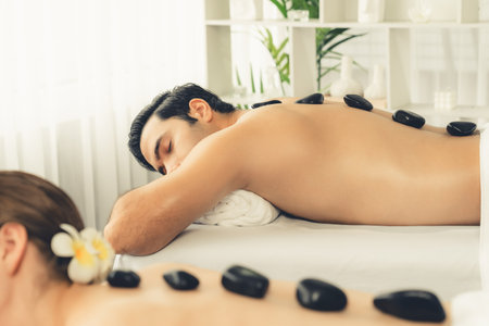 Hot stone massage at spa salon in luxury resort with day light serenity ambient, blissful couple customer enjoying spa basalt stone massage glide over body with soothing warmth. Quiescentの写真素材