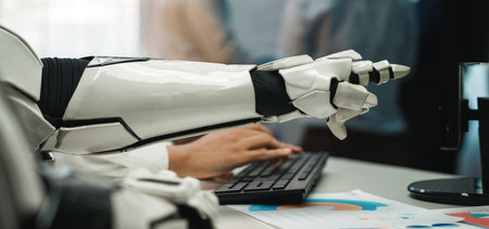 A close-up of a robotic arm interacting with a computer keyboard in a modern office setting, highlighting the blend of technology and human work in the workplace.の写真素材