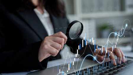 A business professional inspects financial data with a magnifying glass, showcasing charts and statistics on a laptop in a modern office, representing analysis and investment strategy.の写真素材