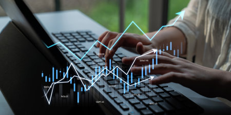 A business professional engages with financial charts and graphs while using a laptop keyboard,...