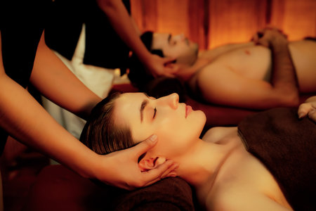 Couple customer enjoying relaxing anti-stress head massage and pampering facial beauty skin recreation leisure in warm candle lighting ambient salon spa in luxury resort or hotel. Quiescentの写真素材