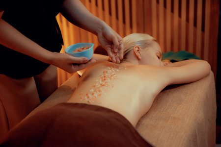 Woman customer having exfoliation treatment in luxury spa salon with warmth candle light ambient. Salt scrub beauty treatment in Health spa body scrub. Quiescentの写真素材