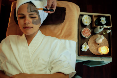 Serene ambiance of spa salon, top view woman customer indulges in rejuvenating with charcoal face cream massage with warm lighting candle. Facial skin treatment and beauty care concept. Quiescentの写真素材