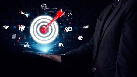 A businessman interacts with a digital tablet featuring a targeted goal visualization. Various icons symbolize success, analytics, and innovative strategies against a dark background.の写真素材