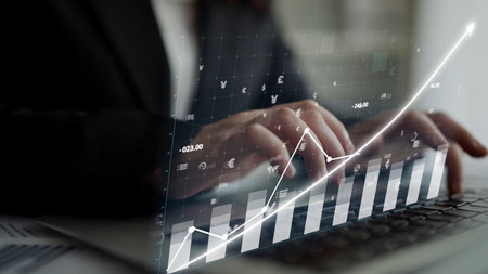 A business professional focuses on data analysis, utilizing digital graphs and charts on a laptop. The modern office environment enhances insights into market performance.の写真素材