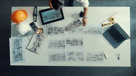 Top down view of engineer looking at tablet while using laptop to analysis building structure....