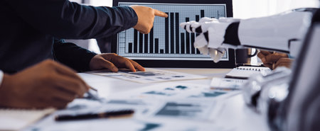 A business team collaborates in a modern office setting, analyzing data presented on a screen, with a focus on trends and strategic planning aided by robotic technology.の写真素材