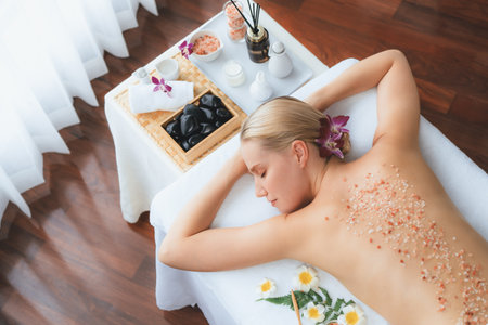 Panorama top view woman customer having exfoliation treatment in luxury spa salon with warmth candle light ambient. Salt scrub beauty treatment in health spa body scrub. Quiescentの写真素材