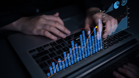 Focused hands work on a laptop displaying graphical data visualization, representing financial...