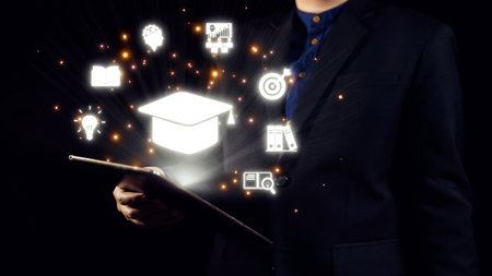 A professional man stands confidently in a dark suit, holding a tablet. Surrounding him are glowing icons representing education, innovation, and knowledge in modern society.の写真素材
