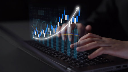 Close-up of a person hands typing on a laptop while analyzing financial graphs and data...