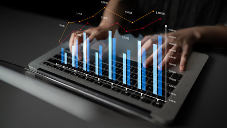 A close-up view of hands typing on a laptop, with visual data graphs overlaying the screen,...