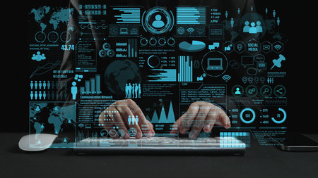 A modern workspace featuring hands typing on a laptop with digital graphics surrounding it,...