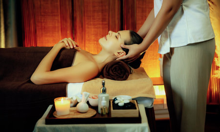 Caucasian woman enjoying relaxing anti-stress head massage and pampering facial beauty skin recreation leisure in warm candle lighting ambient salon spa in luxury resort or hotel. Quiescentの写真素材