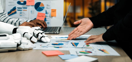 A high-tech business meeting featuring a robotic hand assisting with data analysis on charts and graphs, emphasizing collaboration and innovation in a modern office setting.の写真素材