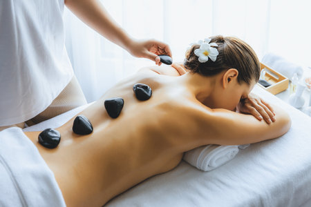 Hot stone massage at spa salon in luxury resort with day light serenity ambient, blissful woman customer enjoying spa basalt stone massage glide over body with soothing warmth. Quiescentの写真素材