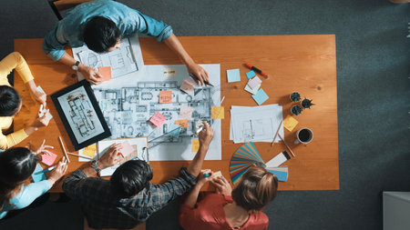 Top down aerial view of smart engineer looking at blueprint at meeting room. Skilled architect team talking and discussing while inspecting at project plan at meeting table with blueprint. Symposium.の写真素材