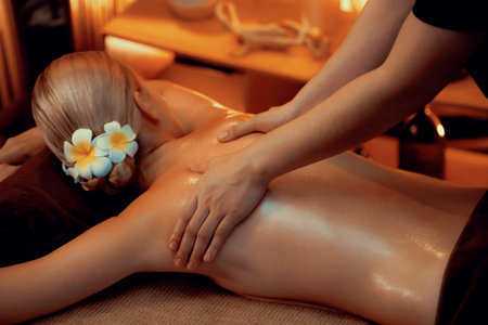 Caucasian woman customer enjoying relaxing anti-stress spa massage and pampering with beauty skin recreation leisure in warm candle lighting ambient salon spa at luxury resort or hotel. Quiescentの写真素材