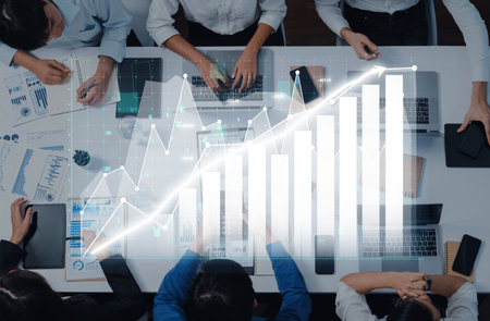 Diverse team collaborates at a modern office table reviewing financial data and market trends while...