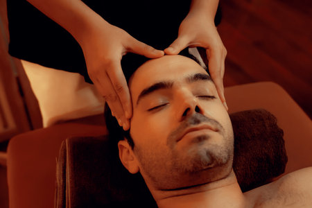 Caucasian man enjoying relaxing anti-stress head massage and pampering facial beauty skin recreation leisure in warm candle lighting ambient salon spa in luxury resort or hotel. Quiescentの写真素材