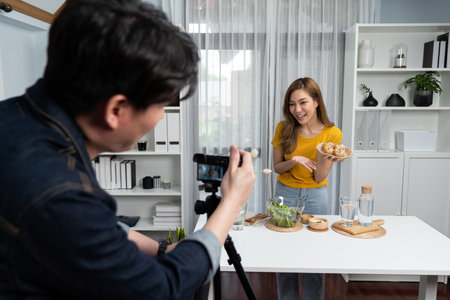 Asian beautiful woman food specialist presenting healthy meal wholegrain bun bread basket on live channel recorded video camera by smart cameraman streaming lifestyle social media online. Infobahn.の写真素材