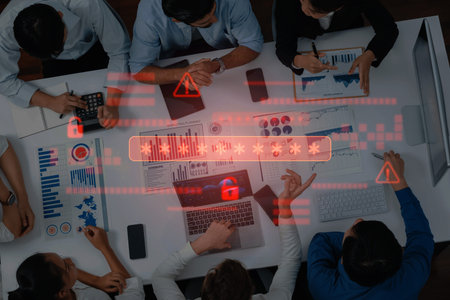 Business professionals gather around a table analyzing financial data and cybersecurity alerts with laptops and charts, emphasizing teamwork and strategic planning.の写真素材