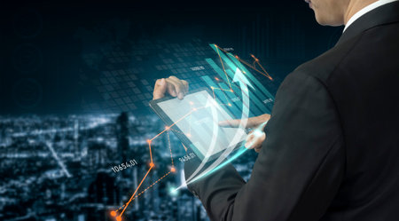 Businessman interacts with a tablet, showcasing digital charts and graphs representing data analysis, growth, and technology against a vibrant city backdrop.の写真素材