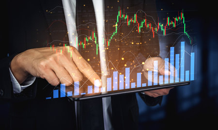 A businessman engages in financial analysis using a tablet. The image highlights stock market charts and data visualization, illustrating investment insights in a modern office.の写真素材