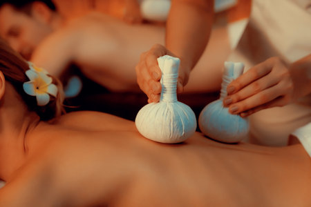Closeup hot herbal ball spa massage body treatment, masseur gently compresses herb bag on couple customer body. Serenity of aromatherapy recreation in warm lighting of candles at spa salon. Quiescentの写真素材