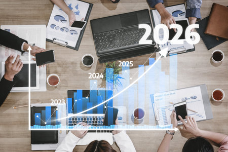 A diverse business team collaborates at a modern office desk, analyzing financial data with graphs projecting growth from 2023 to 2026. Tesselの写真素材