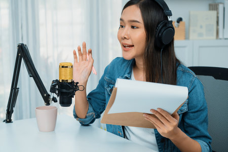 Host channel Asian influencer talking in broadcast streaming online wearing headset on social media live with script note, greeting listeners in life coaching or marketing at modern studio.の写真素材