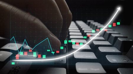 A close-up of a hand on a keyboard, focused on analyzing financial data displayed through graphs and...