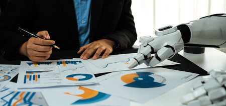 A businessman evaluates financial reports with the aid of a robotic hand, showcasing the merging of technology and human intelligence in a contemporary office setting.の写真素材