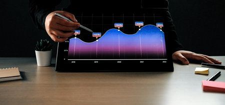 A business professional observes data trends on a digital tablet, showcasing vibrant graphs and...
