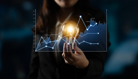 A business professional presents a light bulb, symbolizing innovation, against a backdrop of a financial data chart, illustrating modern corporate strategy and analytics.の写真素材