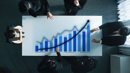 A business team gathers around a table, engaging in a strategy session focused on growth, as illustrated by a prominently displayed upward trend graph.の写真素材