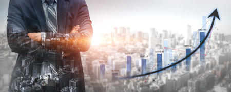 Confident businessman stands with arms crossed, overlooking a city skyline. A growing graph illustrates trends in financial investment and economic progress, symbolizing success.の写真素材