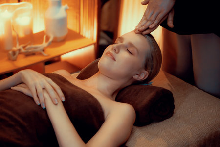 Caucasian woman enjoying relaxing anti-stress head massage and pampering facial beauty skin recreation leisure in warm candle lighting ambient salon spa in luxury resort or hotel. Quiescentの写真素材