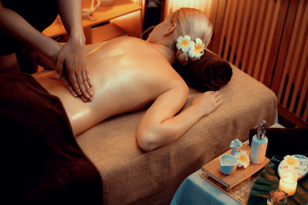 Caucasian woman customer enjoying relaxing anti-stress spa massage and pampering with beauty skin recreation leisure in warm candle lighting ambient salon spa at luxury resort or hotel. Quiescentの写真素材