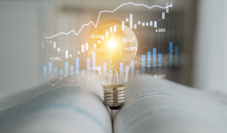 A glowing light bulb rests on an open book, symbolizing knowledge and innovation, surrounded by financial charts and growth indicators for educational themes.の写真素材