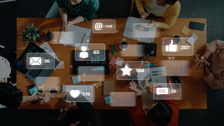 Aerial view of a collaborative workspace showing people engaged in discussions with digital social media icons and metrics highlighting communication and teamwork. Rasterの写真素材