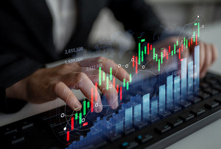 A business professional closely analyzes financial data and stock market trends using digital graphs and tools on a keyboard in a modern office setting.の写真素材