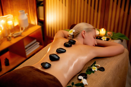 Hot stone massage at spa salon in luxury resort with warm candle light, blissful woman customer enjoying spa basalt stone massage glide over body with soothing warmth. Quiescentの写真素材