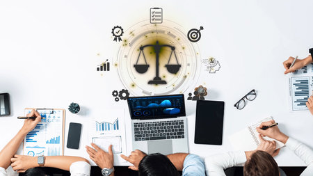 Diverse professionals engage in a collaborative strategy session, using a laptop and notebooks, surrounded by charts and icons symbolizing balance and justice in the workplace. Rasterの写真素材