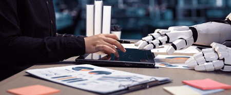 A human hand interacts with a tablet alongside a robotic hand, emphasizing the blend of technology...