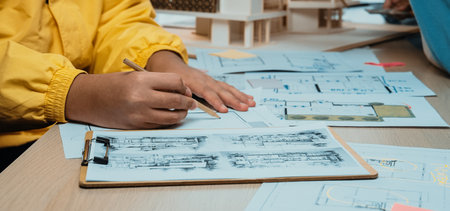An architect focused on sketching detailed designs and plans at a work table filled with drawings, models, and creative materials. Collaboration and inspiration evident.の写真素材