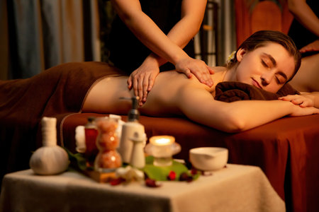 Caucasian couple customer enjoying relaxing anti-stress spa massage and pampering with beauty skin recreation leisure in warm candle lighting ambient salon spa at luxury resort or hotel. Quiescentの写真素材